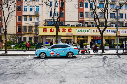 Shanghai, China - Bustling street in Pudong with blue Doraemon-themed car parked near small cafes and shops. Residential buildings with beige-orange facades in background