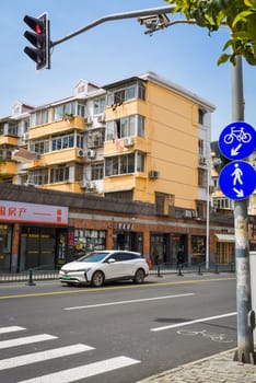 Shanghai, China - 1 April 2025: Street view in Pudong district with old residential building, wine bar, electric car, traffic light and bicycle lane signs