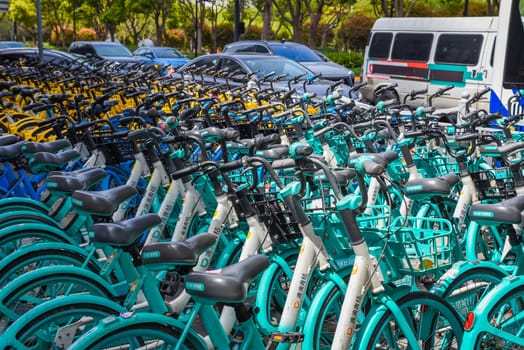 Shanghai, China - 1 April 2025: Blue rental bikes parked in urban area. Empty parking lot with cars visible. No people. Clear day