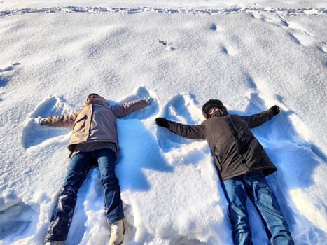 Friends enjoy a playful winter day as they lie on the snow and create snow angels, surrounded by a bright and clear blue sky, showcasing the joy of the season.