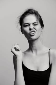 Playful young woman with messy hair making a funny face and clenched fist, evoking a sense of joy and spontaneity in a minimalist black and white setting.