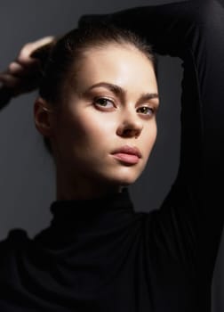 Portrait of a beautiful young woman showcasing elegance and confidence, her hair styled back, against a moody dark backdrop. Emphasizes fashion and modern beauty.