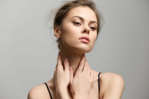 A stylish female model expresses poise and confidence with her hands around her neck, emphasizing her elegant features against a smooth gray backdrop.