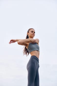 Athletic woman in trendy sportswear stretching against a soft grey sky, representing health, fitness, and an active lifestyle, ideal for wellness focused projects and campaigns