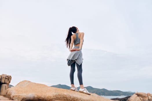 An athletic woman in snug workout gear, stretching happily on rocky ground during outdoor exercise The scenic backdrop features soft colors in a calm, inviting environment