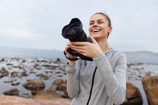 A joyful young woman dressed in a gray jacket is photographing the scenic coastal landscape Her happiness shines as she enjoys her passion for photography by the sea