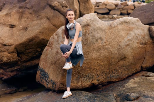 Fit young woman wearing trendy sportswear, resting on a rock in a natural setting, embodying a healthy lifestyle and fitness Perfect for wellness and sports themes