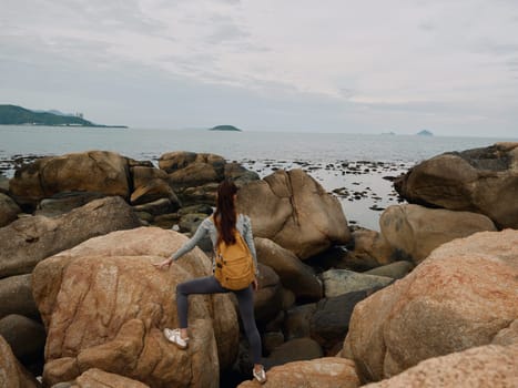 A young woman in activewear stands on rocks by the sea, capturing the spirit of adventure and exploration in a natural coastal landscape