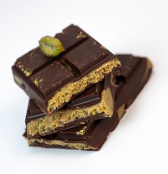 Stacked layers of kadaif embrace a generous coating of rich chocolate and are topped with a pistachio, showcasing the delightful texture and flavors in a culinary presentation.