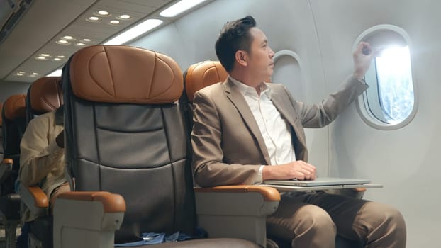 Professional Asian businessman working with notebook computer while sitting inside an airplane, business man working with laptop in aircraft cabin during his business travel
