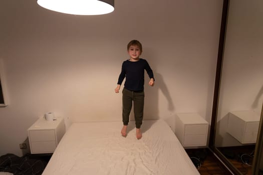 Playful child jumping on bed in bedroom, enjoying playtime at home