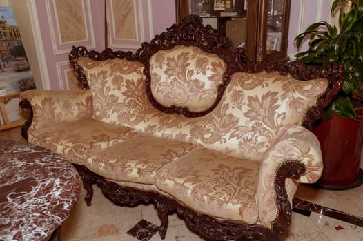 An ornate gold beige sofa with silk upholstery, gold accents and intricate carvings on the wood inserts. The luxurious design makes it a striking feature for luxuriously decorated rooms.