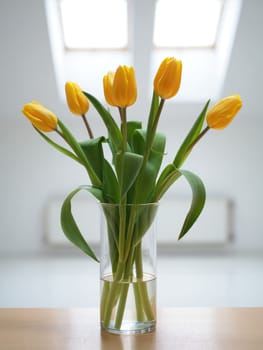 A beautiful bouquet of vibrant yellow tulips stands gracefully in a clear glass vase.