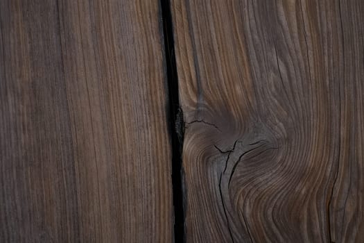 Detailed close up of a wooden surface featuring a noticeable crack and intricate grain patterns. The rich textures highlight the woods natural beauty and uniqueness.
