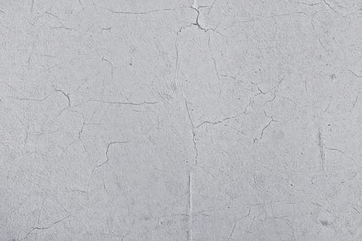 A gray surface displays a textured appearance with varying cracks and imperfections. This minimalist backdrop showcases variations in color and texture, highlighting its raw aesthetic.