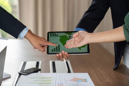 In a modern office setting, a diverse team emphasizes ESG discussions while analyzing data on a tablet, highlighting teamwork and sustainability strategies.