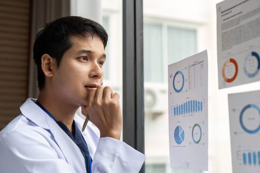 A focused doctor reviewing data and statistics on charts in a hospital, reflecting on insights that lead to better patient outcomes.
