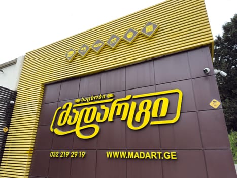 Tbilisi, Georgia, April 13, 2025: Facade of Madart pastry shop in Georgia with bright yellow logo in Georgian script, website address and dessert icons above entrance