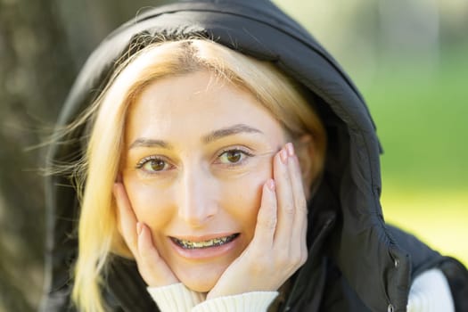 Portrait of a blonde woman wearing braces and holding her face with hands