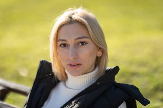 Blonde woman relaxing outdoors in nature wearing white turtleneck and black vest