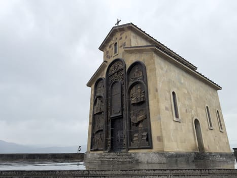 Tbilisi, Georgia, April 13, 2025: Church of Saint Virgin Mary near Chronicle of Georgia monument in Tbilisi. Stone facade with bronze bas reliefs seen on rainy day under cloudy sky