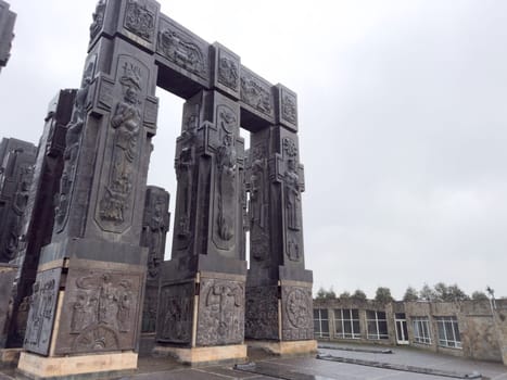 Tbilisi, Georgia, April 13, 2025: Massive stone columns of the Chronicle of Georgia monument stand tall against grey sky in Tbilisi. Intricate bas reliefs depict historical and religious scenes