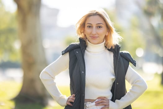 Portrait of a confident young woman standing in a park with her hands on her hips, enjoying the pleasant weather