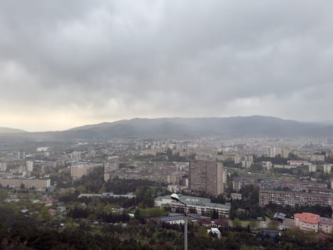Overcast panoramic view of Tbilisi, Georgia with dense Soviet-era apartment blocks and modern buildings under cloudy sky. Urban atmosphere of Caucasus capital city with mountain backdrop