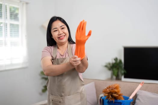 A cheerful woman gets ready to clean her home, smiling as she puts on bright orange rubber gloves, showcasing her positive approach to household chores.