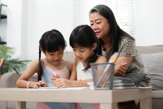 A loving grandmother helps her granddaughters with their drawing and writing activities, fostering creativity and learning in a warm home environment.