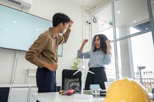 Two young professionals celebrate their successful planning session focused on sustainable housing solutions, showcasing their enthusiasm and teamwork.
