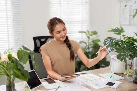 A woman analyzes data in a green office, focusing on ESG sustainability efforts with her tablet and thoughtful expression.