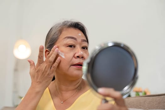 This image captures a mature woman applying cream to her face, showcasing her skincare routine and the beauty of aging gracefully.