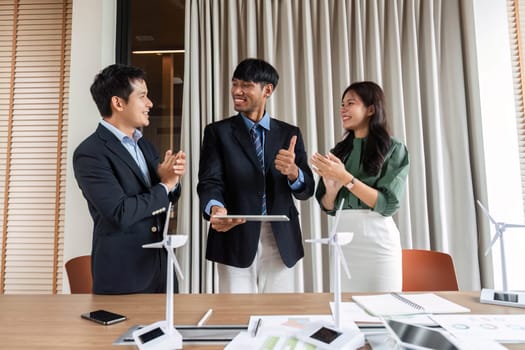 In a bright modern office, a diverse team celebrates successful ESG collaboration, expressing enthusiasm and positive energy after a productive meeting.
