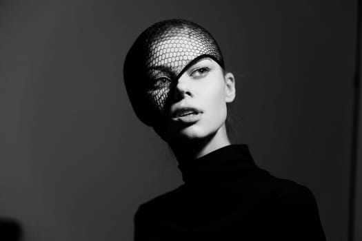 Captivating black and white image of a fashionable model showcasing a bold look with a mesh head covering, emphasizing her sophisticated features and artistic style.