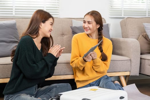 Two friends sharing travel ideas on a tablet, smiling and enjoying each other's company while sitting comfortably on the floor.