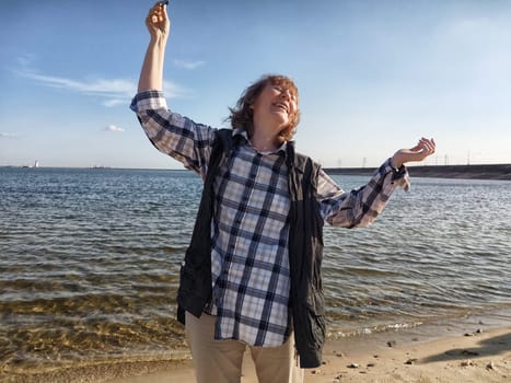 Blonde woman shares her joy on a beach, celebrating life and her travel experiences during a sunny excursion by the water.