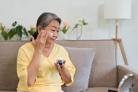 A mature woman enjoys applying moisturizer, highlighting the importance of skincare and embracing beauty at any age.