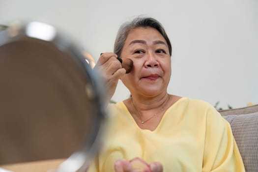 A confident older woman enhances her features with makeup, celebrating age diversity and self-care in a comfortable home environment.