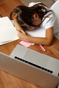 tired little child girl using laptop for studying online. the child put her head down on the table to rest. hard to learn online at home