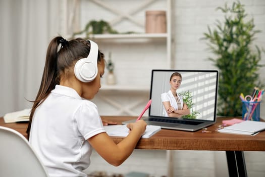little child girl in headphones have video call with teacher using laptop for studying online. online lesson at home. online video call with teacher
