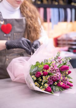 Florist packs beautiful flower arrangement of pink tulips, wax flower, chamomile, eucalyptus - stylish gift for Valentine's Day. Vertical. Close-up.