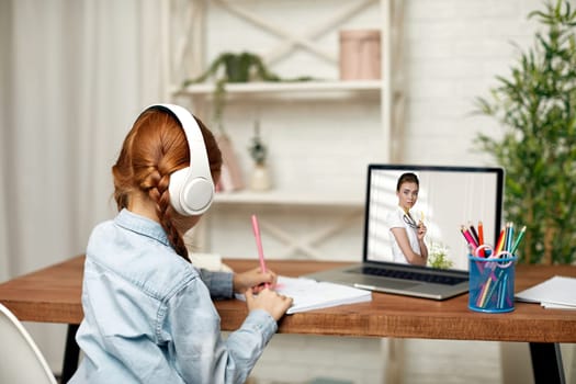 happy little child girl in headphones using laptop for studying online learning system. online lesson at home. online video call with teacher