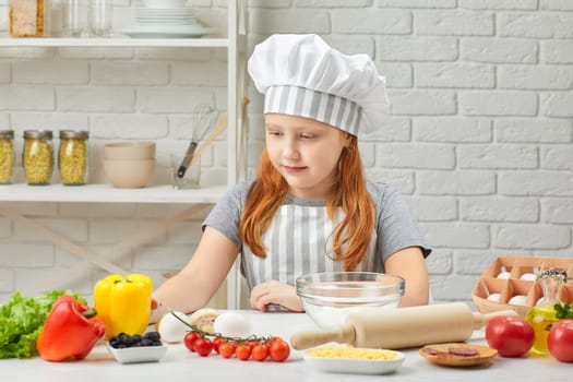 happy little girl in chef hat and an apron cooking pizza in the kitchen.
