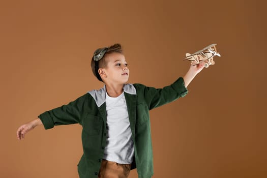 happy child boy playing with wooden toy airplane on studio background. kid dreams of traveling