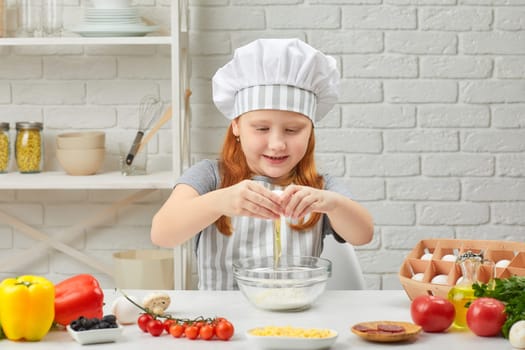 cute little girl in chef hat and an apron is breaking yellow egg into fresh dough in the kitchen. child cooking with dough