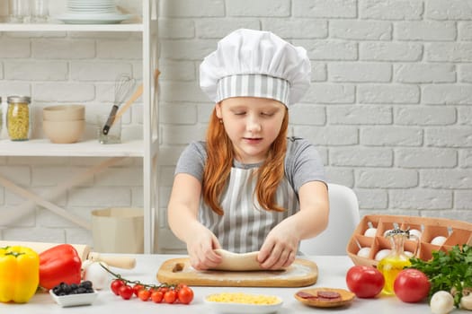 little child girl in cap and an apron knead the dough in the kitchen