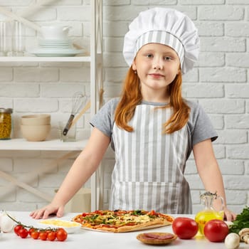 little girl in chef hat and an apron cooking pizza in the kitchen.