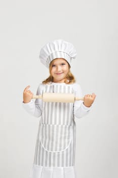 smiling little girl in chef hat and apron holding rolling pin. child dreams of becoming a chef