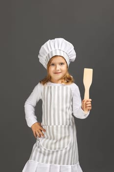 cute little girl in chef hat and apron preparing healthy meal on gray background. child dreams of becoming a chef